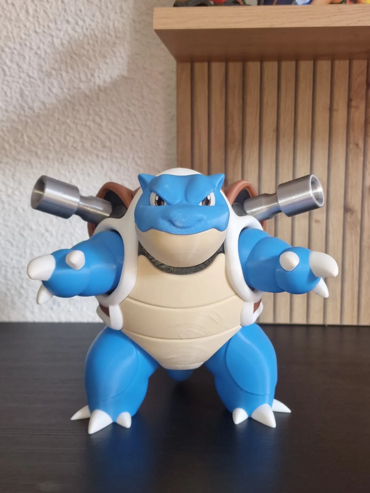 Figura de Blastoise de frente, cuerpo azul y vientre crema, con los dos cañones metálicos desplegados sobre los hombros